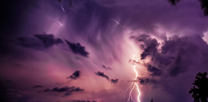 Purple sky with dark clouds and a bright lightning bolt striking down.