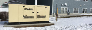 Kohler generator installation placed outdoors next to a building, surrounded by snow-covered ground.