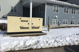 Kohler generator installation placed outdoors next to a building, surrounded by snow-covered ground.