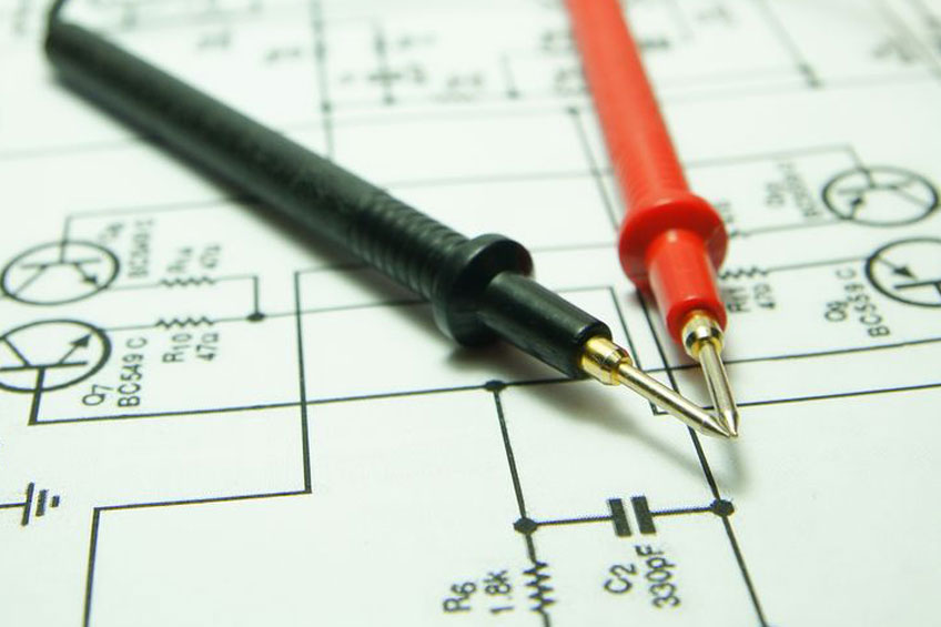 Two multimeter probes, one black and one red, placed on a printed electronic circuit diagram.